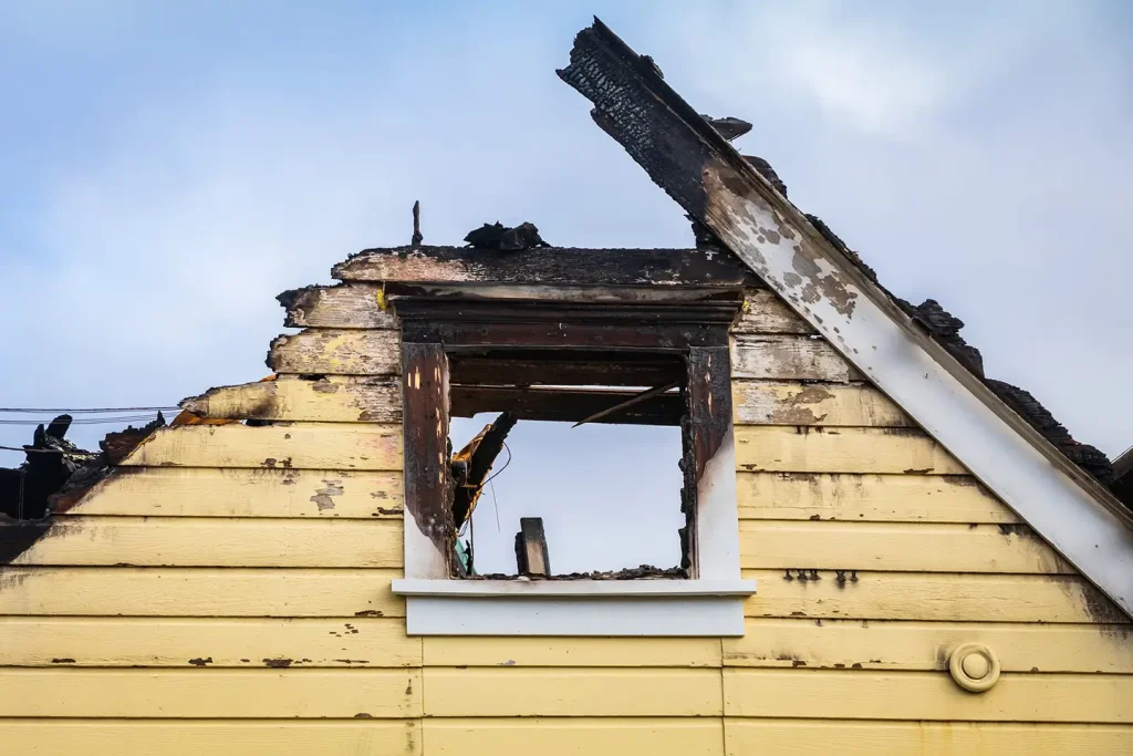 Partially burnt yellow house siding with exposed, blackened wooden beams after a disaster