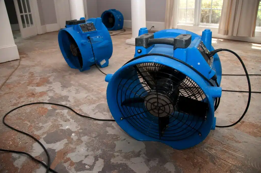 Water damage restoration team drying a floor with industrial fans and equipment.